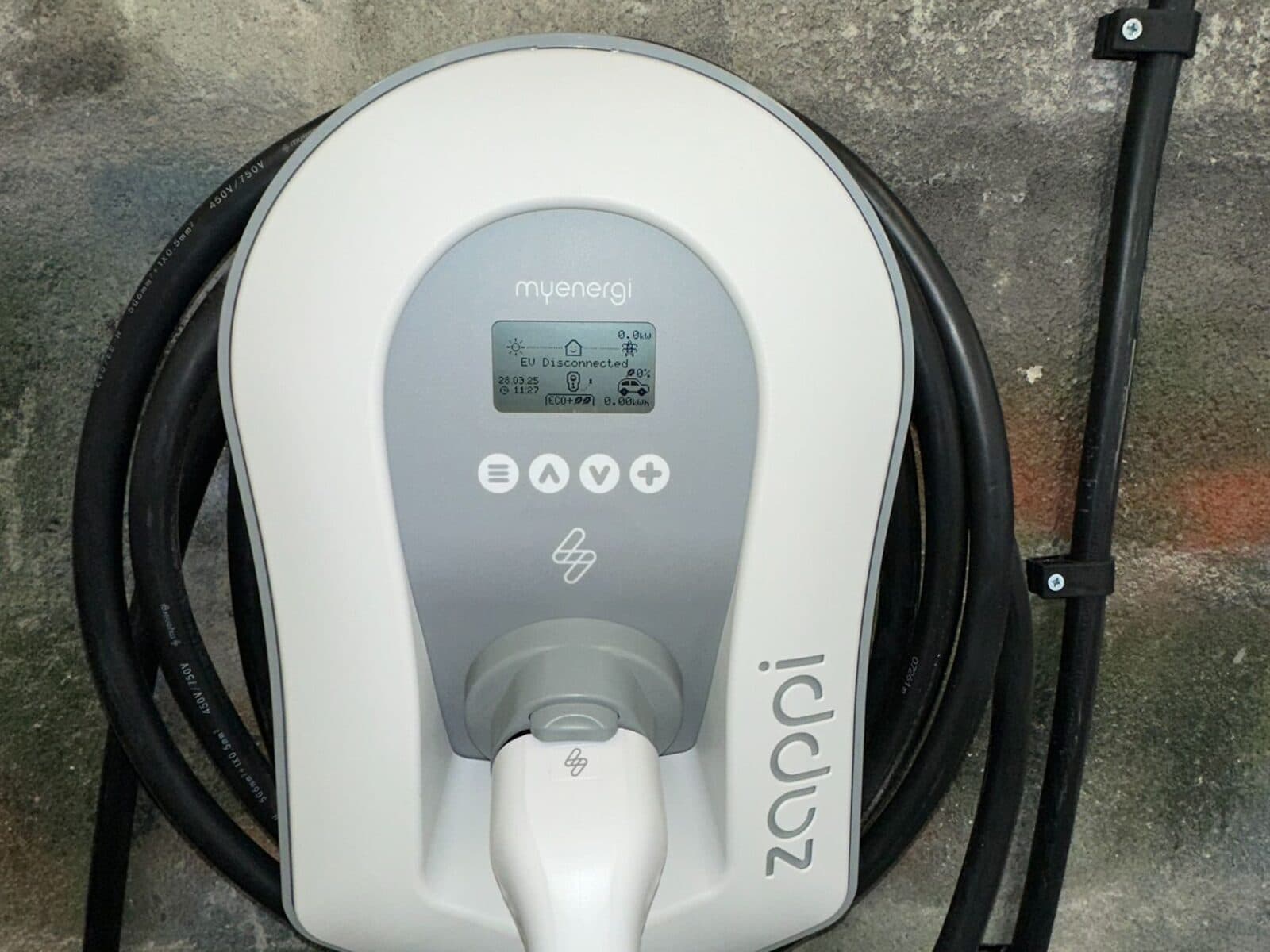White zappi home car charger fitted to a stone wall with its cable neatly coiled