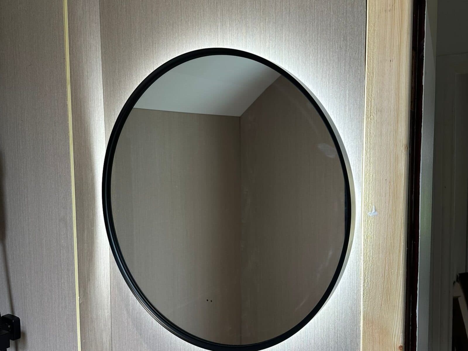 Round backlit mirror glowing on a bathroom wall
